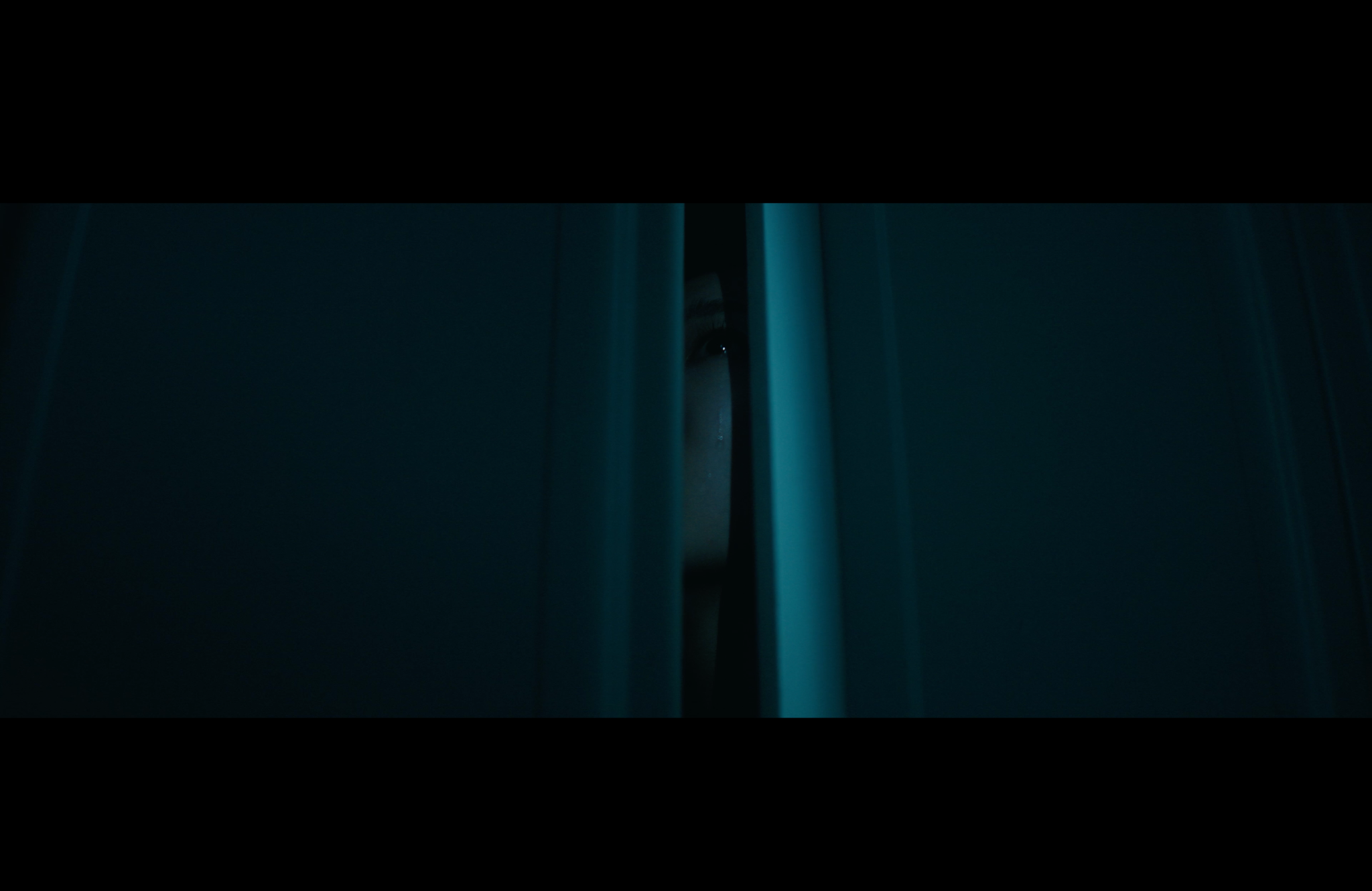 An eye watches through a narrow opening in the dark