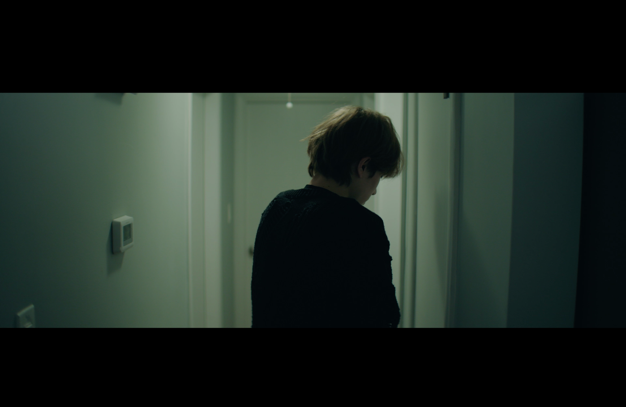 A figure stands in a dimly lit hallway